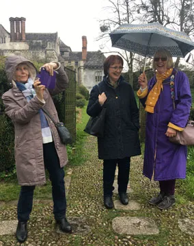 three ladies out in the rain with raincoats and umbarella, smiling