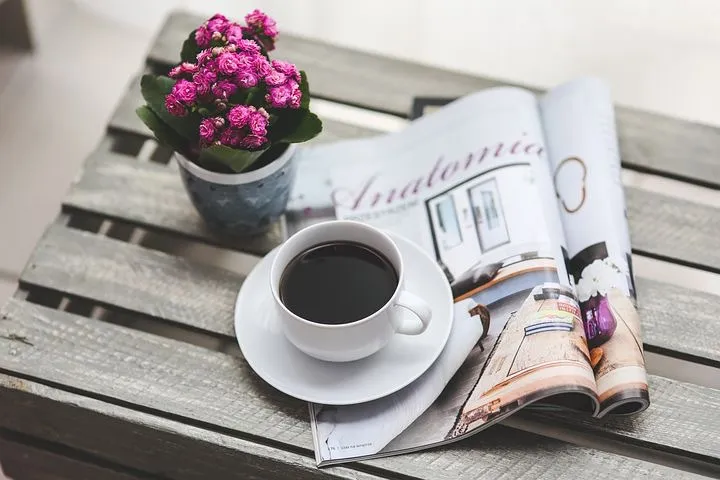 cup of coffee on a table with newspapers and pot of flowers